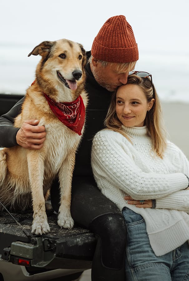 Man, woman and dog sitting by beach in truck bed smiling