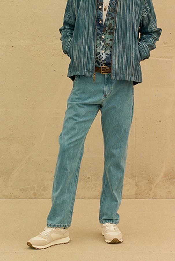Man standing near wall wearing lightwash jeans and patterned jacket